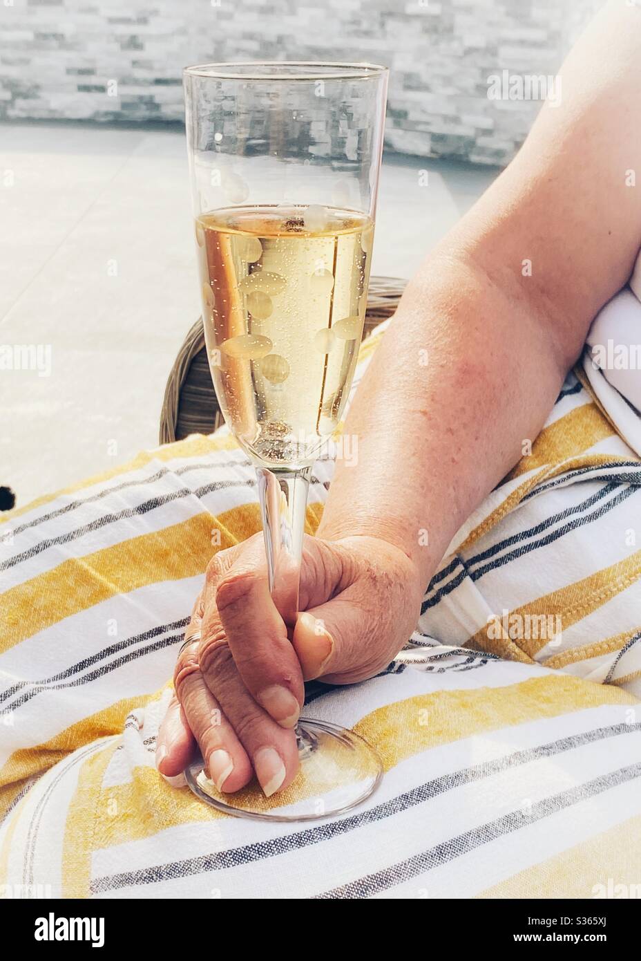 Person, die an einem Sommerabend ein Glas Champagner mit Flöte in einem Garten hält Stockfoto