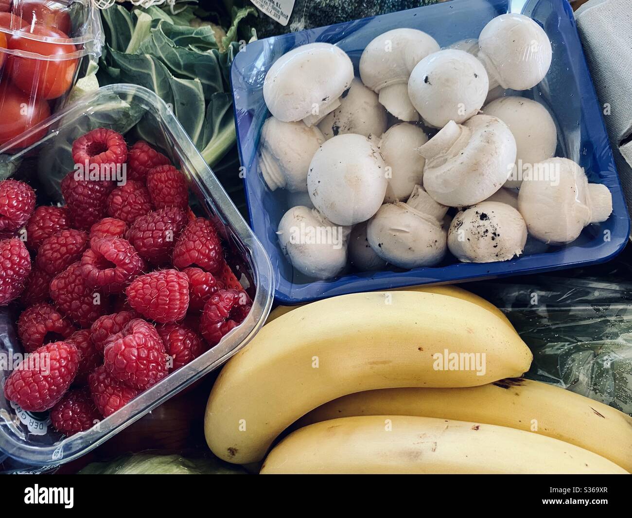 Nahaufnahme von frischem Obst und Gemüse, das den Rahmen mit gesunden Farben füllt. Himbeeren, Bananen, Pilze und Salatgemüse in einer Kiste mit gemischten Früchten und Gemüse. Stockfoto