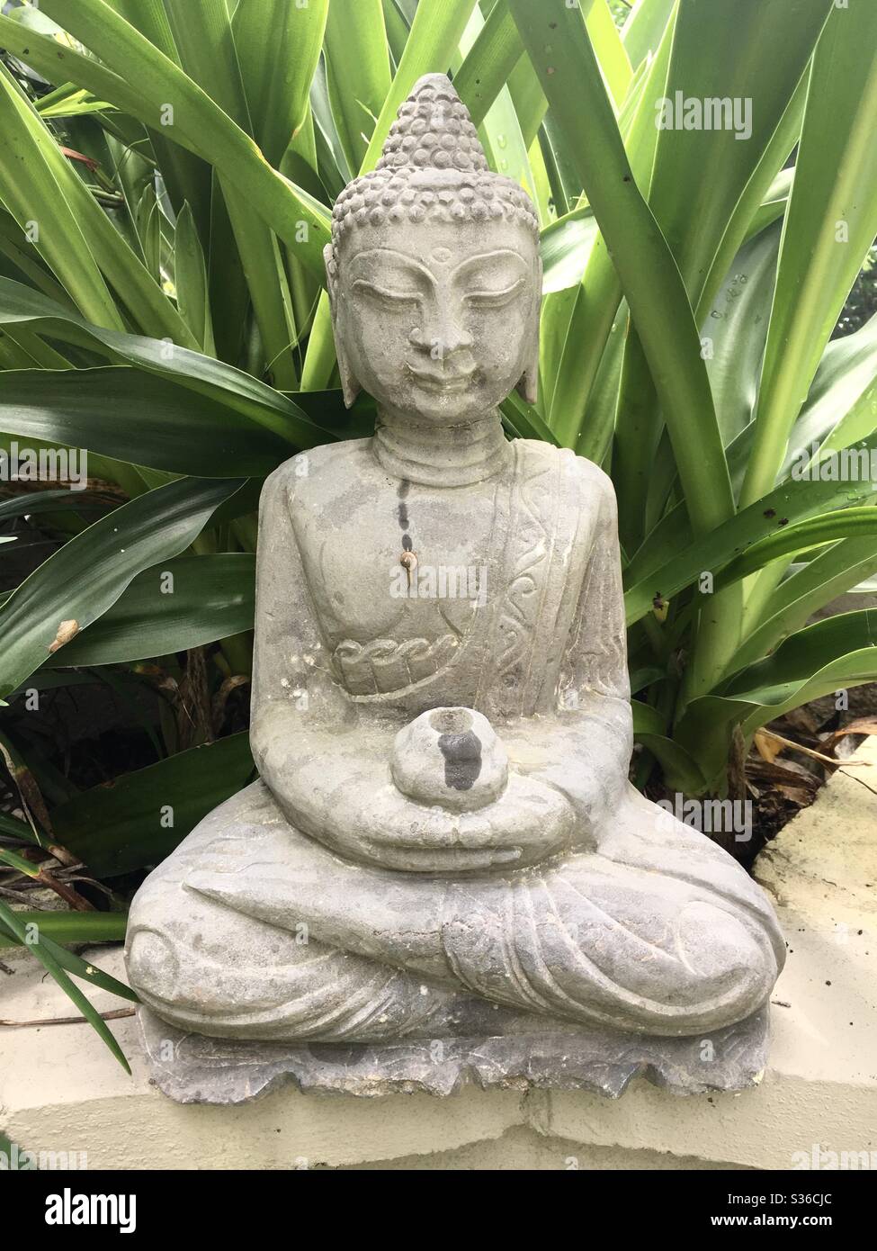 Buddha, der Meister aller Lebewesen, sowohl großer als auch kleiner. Eine Steinskulptur Buddhas mit einer kleinen Schnecke, die an seiner Vorderseite entlang gleitet. Stockfoto