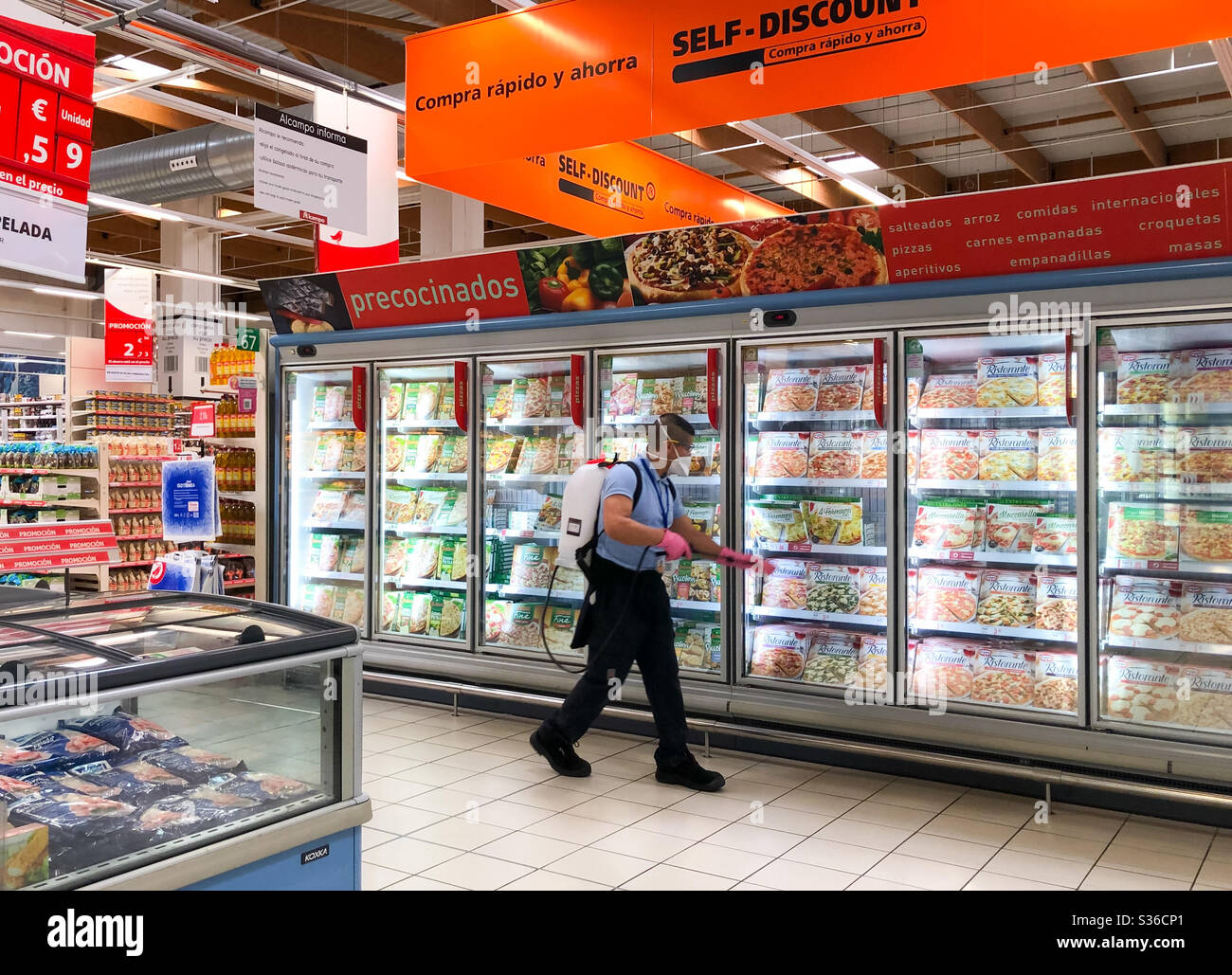 Alicante, Spanien - April 2020: Arbeiter, die Kühlschränke in Alcampo (Auchan) mit Sprühgeräten desinfizieren Stockfoto