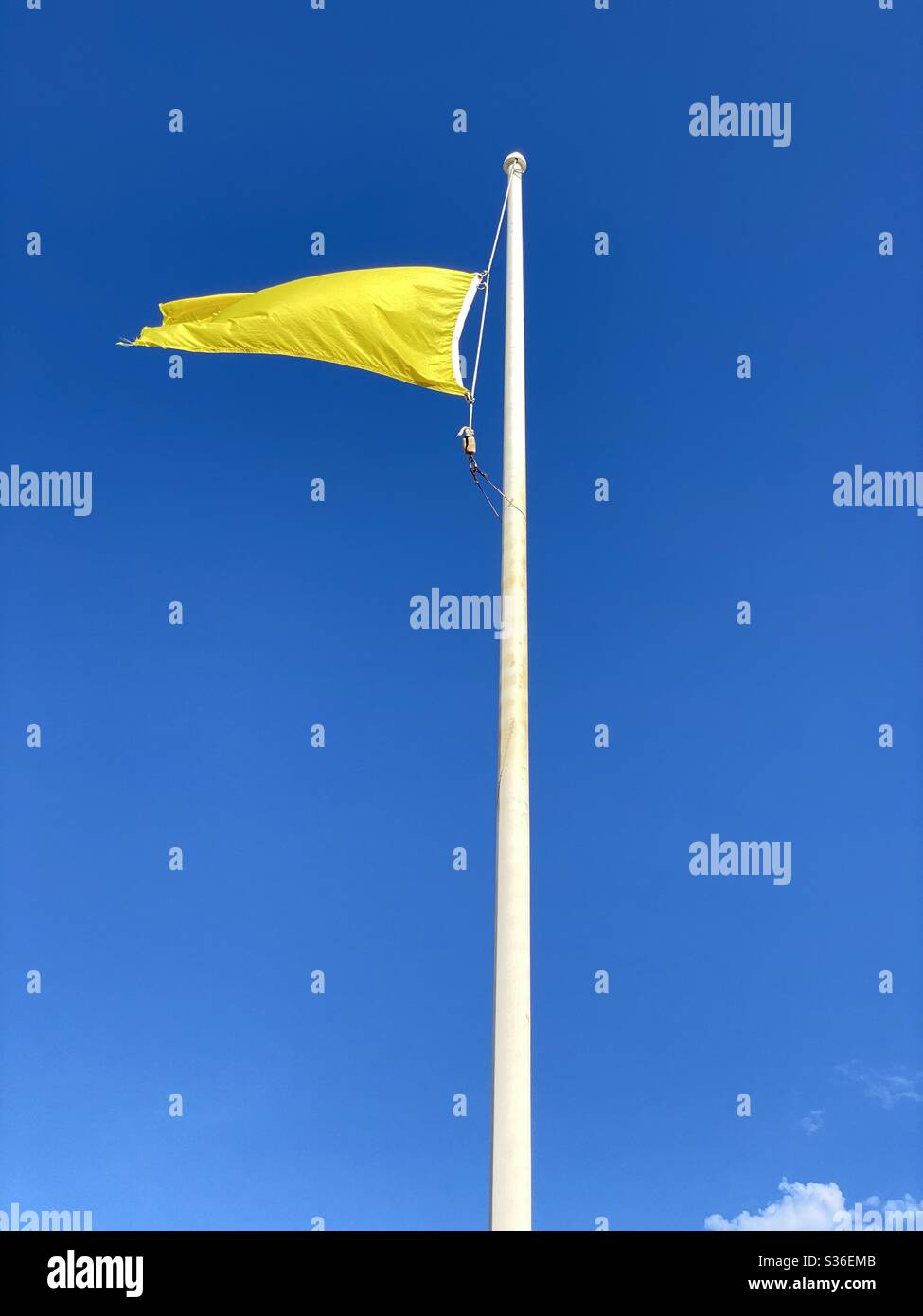 Leuchtend gelbe Flagge und Stange fliegen am Strand mit klarem blauen Himmel Hintergrund Stockfoto