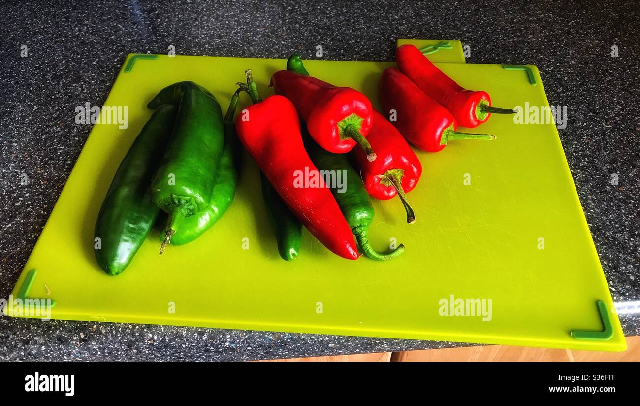 Grünes Schneidebrett mit roten und grünen Chilis darauf Stockfoto