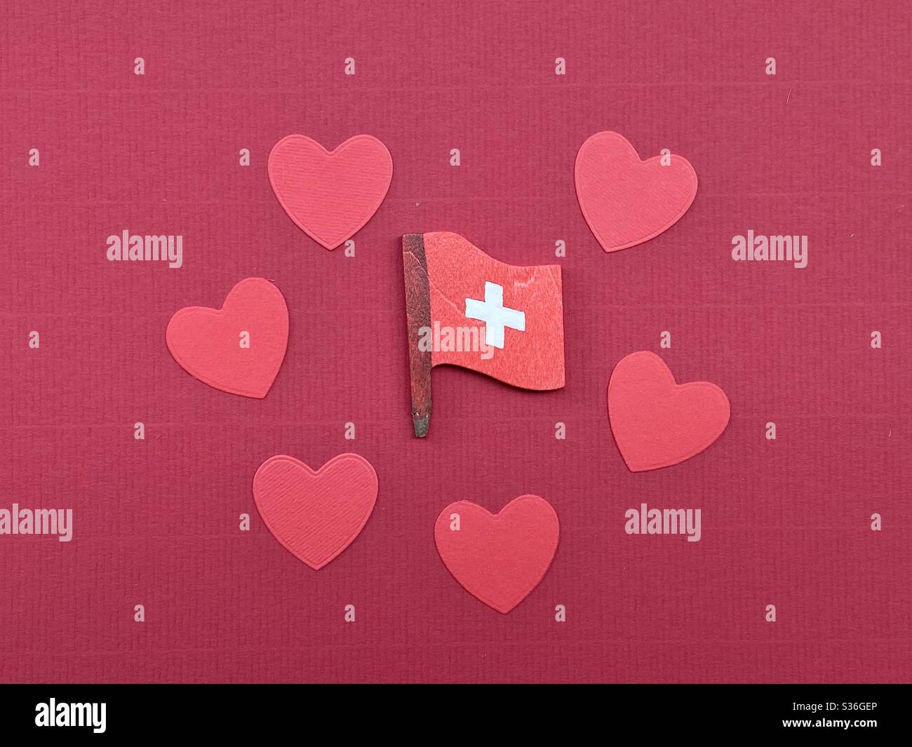 Love Switzerland mit einer Komposition oder roten Papierherzen und einem handgefertigten Schweizer Flaggendesign aus Holz über roter Farbe Stockfoto