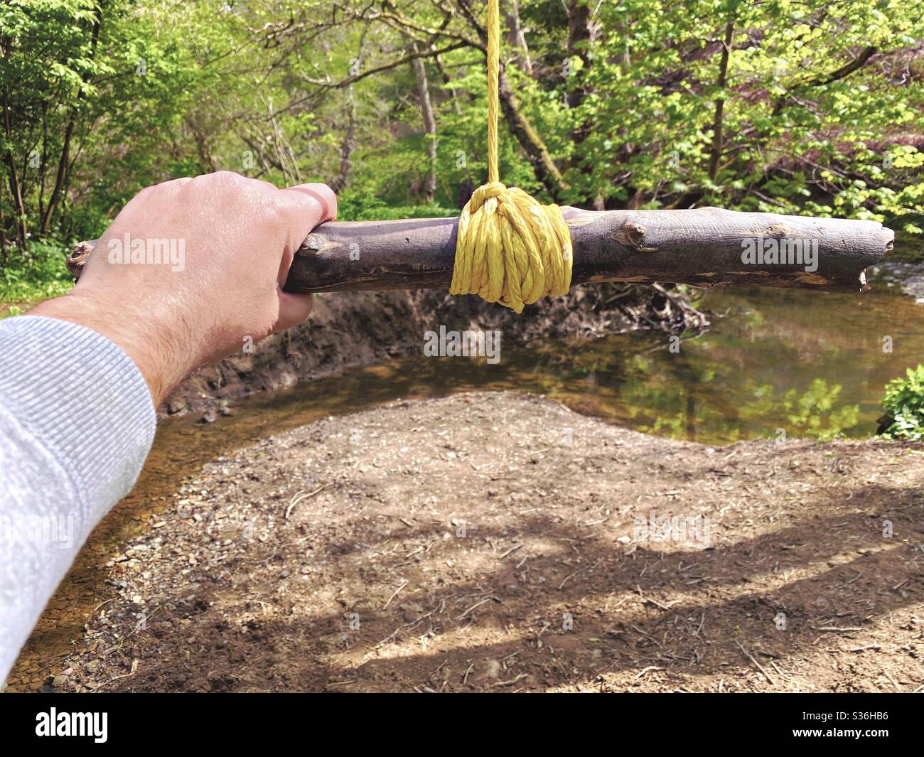 Nahaufnahme von Details eines Mannes, der an einer Seilschaukel hält, die an den Zweigen eines reifen Baumes in einem Wald hängt. Ein kleiner Stab wird mit Knoten als Bügel gebunden, um über Fluß unten zu schwingen Stockfoto