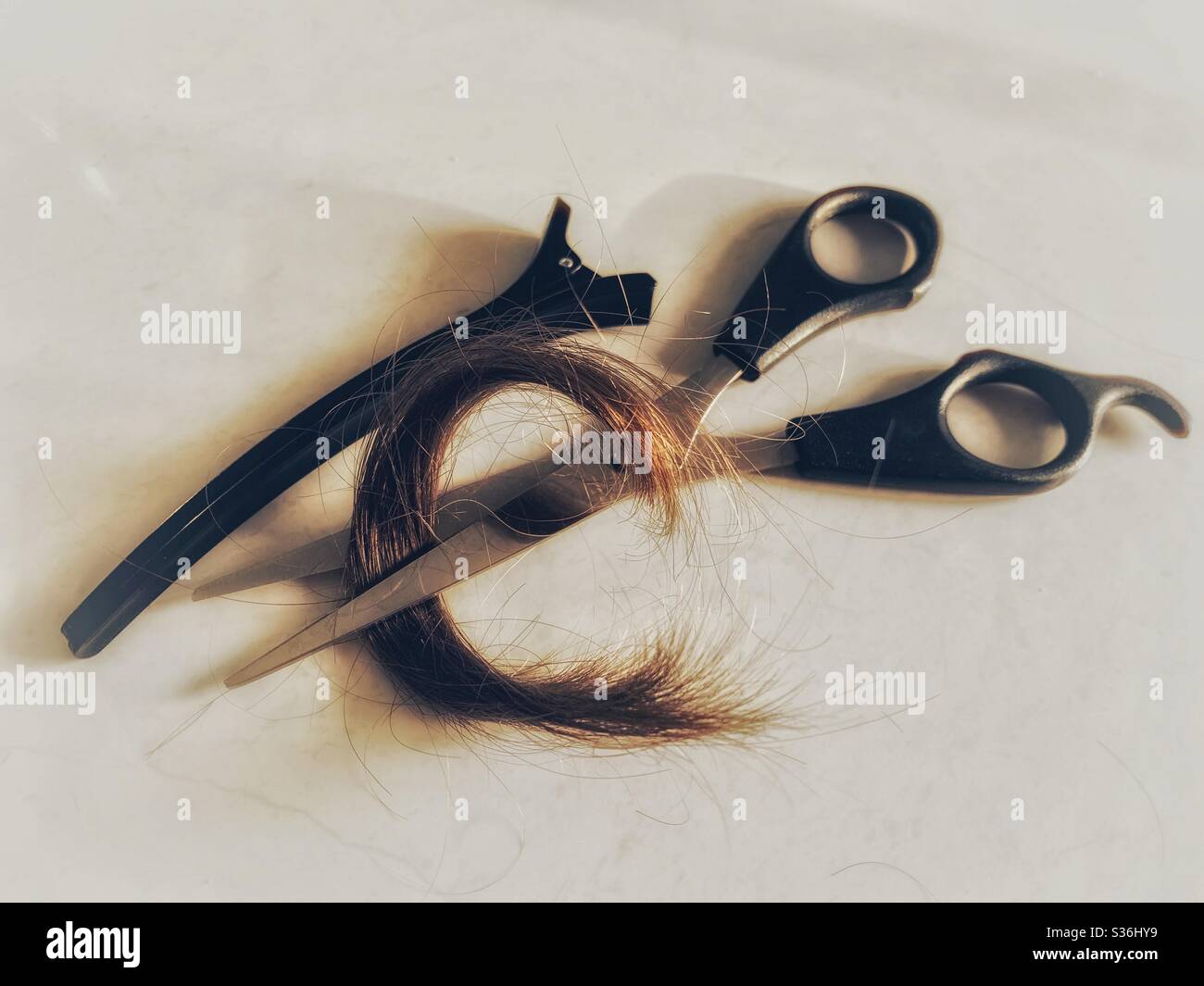 Friseurschere und eine braune Haarsträhne - Smartphone-aufgenommenes Stockfoto
