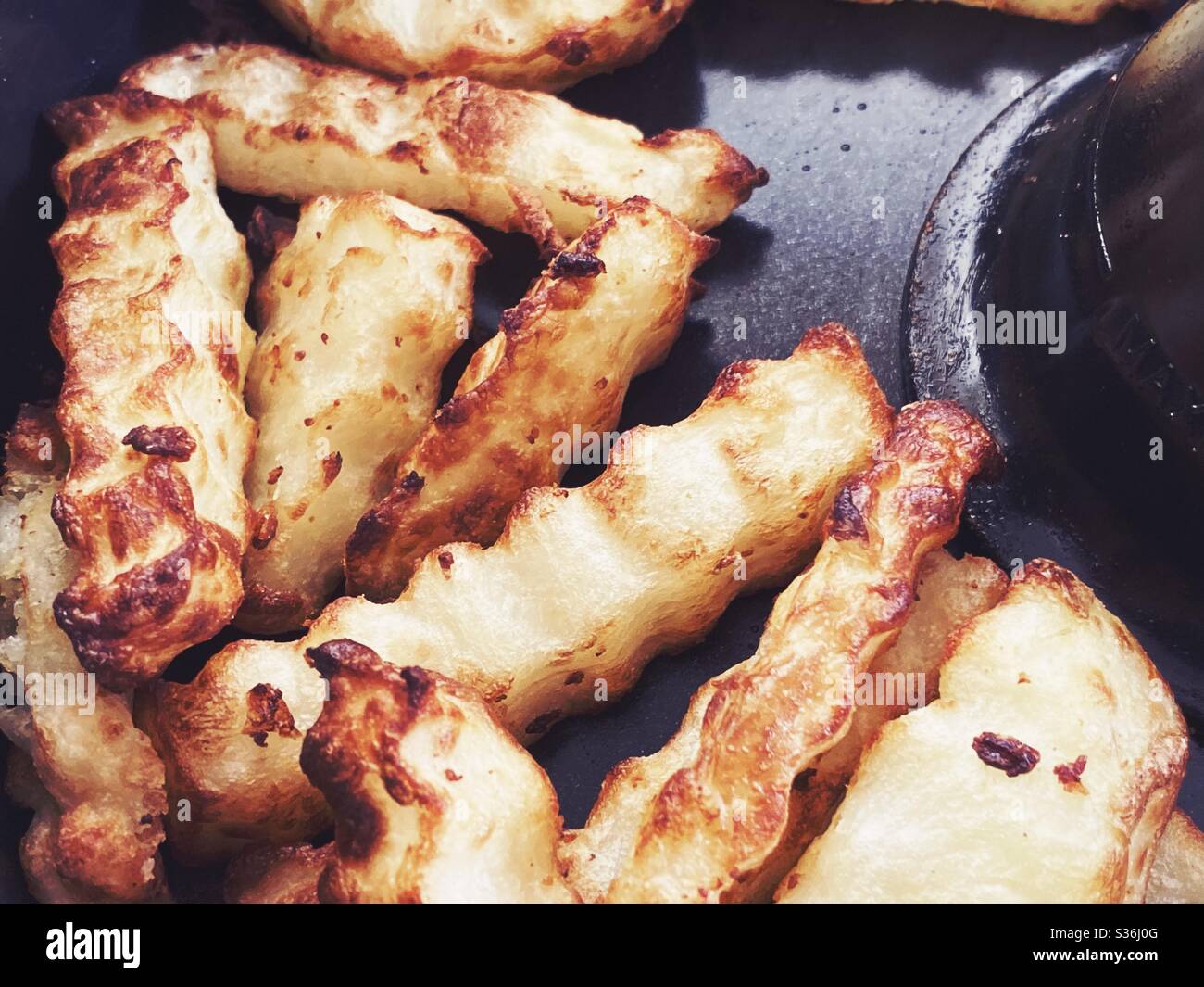 Nahaufnahme der in der Pfanne einer rotierenden Fritteuse geschnittenen Pommes frites. Hausgemachte Pommes frites mit einem in heißer Luft gebratenen Crinkle Cutter, eine gesündere Art zu kochen. Knusprige Kartoffelchips zum Abendessen. - Smartphone-aufgenommenes Stockfoto