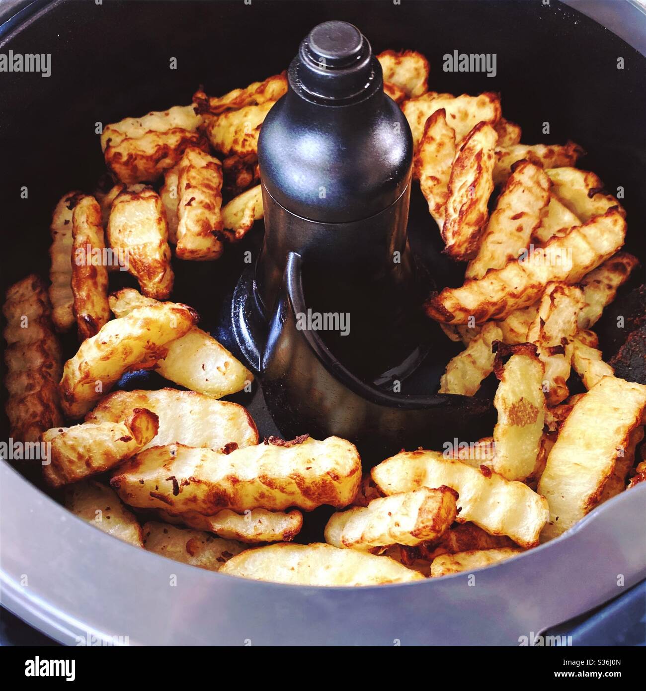 Nahaufnahme der in der Pfanne einer rotierenden Fritteuse geschnittenen Pommes frites. Hausgemachte Pommes frites mit einem in heißer Luft gebratenen Crinkle Cutter, eine gesündere Art zu kochen. Knusprige Kartoffelchips zum Abendessen. - Smartphone-aufgenommenes Stockfoto