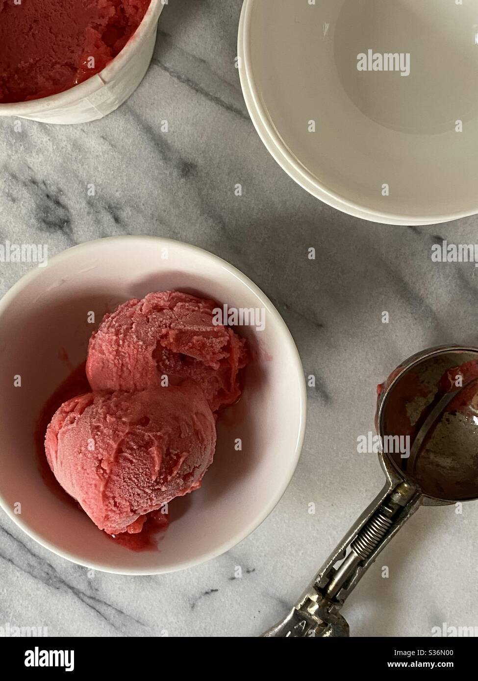 Himbeer-Eis in Schüssel mit Schaufel in Marmor Arbeitsplatte - Smartphone-aufgenommenes Stockfoto