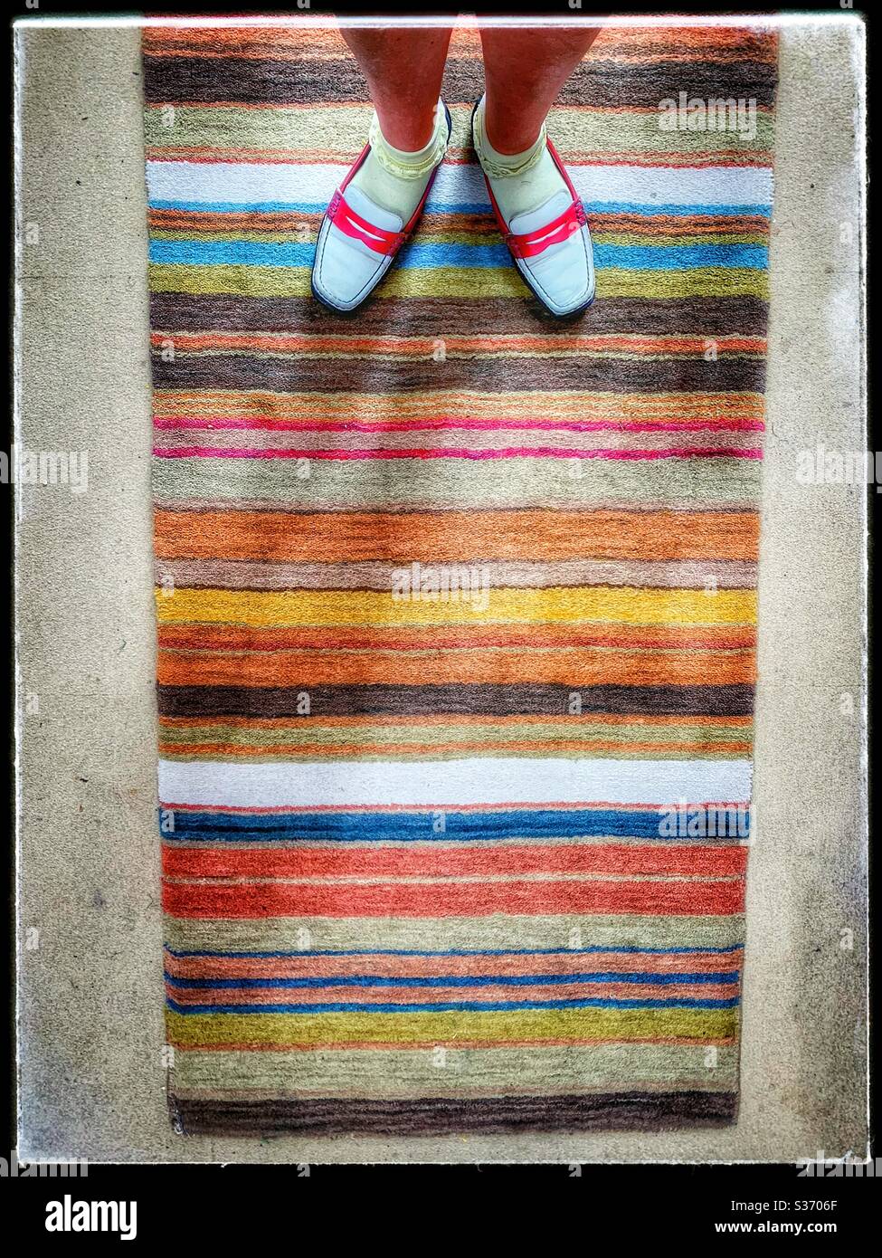 Regenbogenfarbener Teppich mit einem Paar roter, weißer und blauer Schuhe Stockfoto