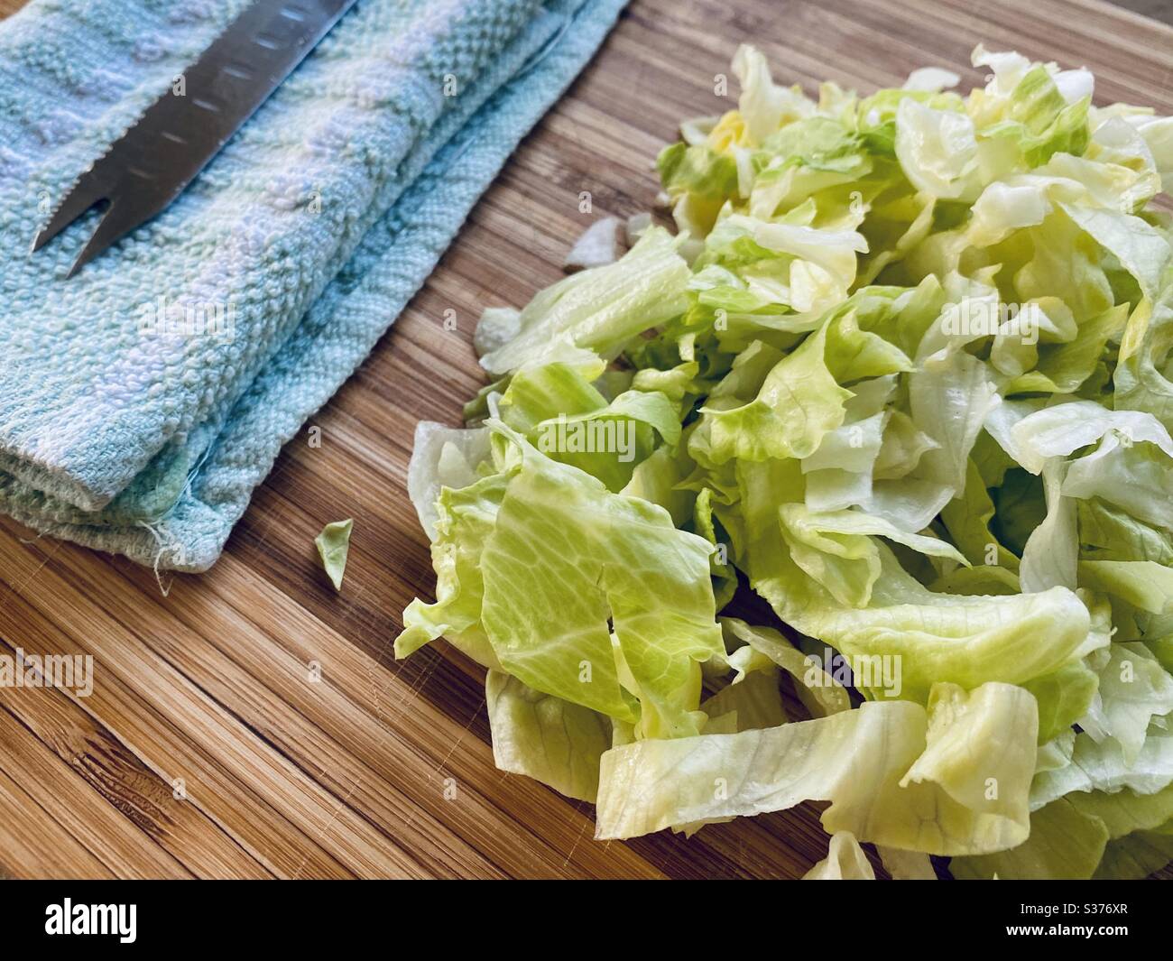 Nahaufnahme von gesundem Salat auf einem rustikalen Holzschneidebrett in der Küche mit gezacktem Messer gehackt. Einen Salat zum Abendessen zubereiten. - Smartphone-aufgenommenes Stockfoto