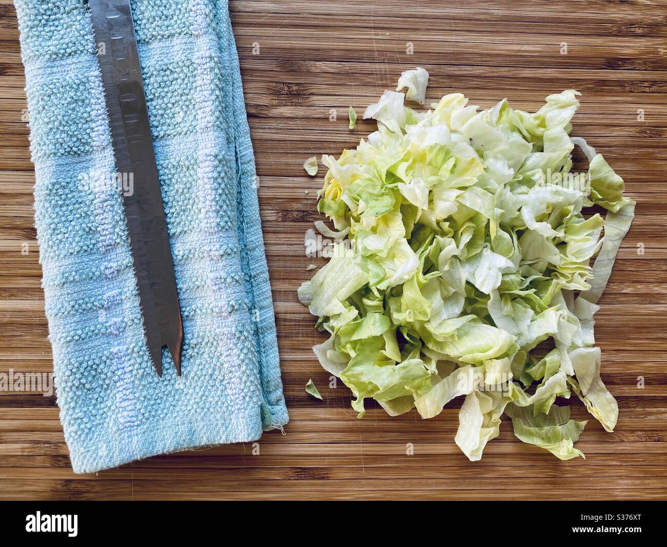 Nahaufnahme von gesundem Salat auf einem rustikalen Holzschneidebrett in der Küche mit gezacktem Messer gehackt. Einen Salat zum Abendessen zubereiten. - Smartphone-aufgenommenes Stockfoto