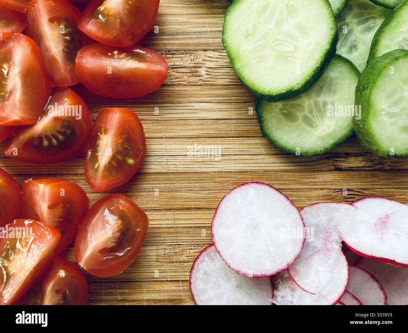 Nahaufnahme von frisch zubereiteten Salatzutaten zum Abendessen. Gesunde Tomaten, Rettich und Gurke. Gewaschen und gespült. Geschnitten, gehackt und geviertelt auf einem rustikalen Holzbrett Stockfoto