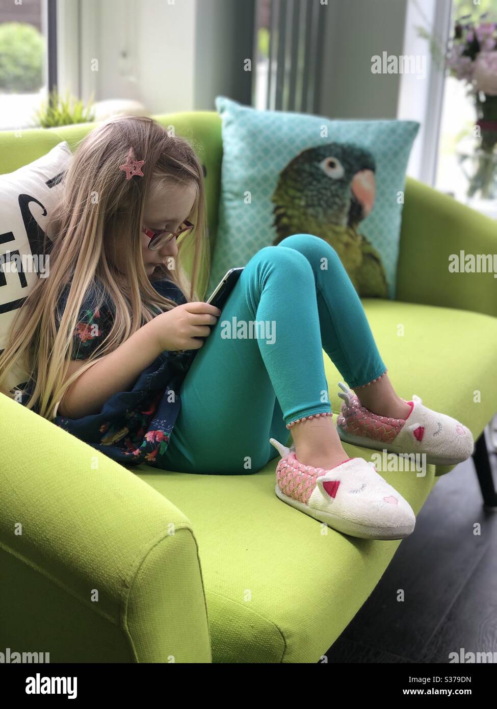 Kleines Mädchen auf buntem Sofa sitzen und mit digitalem Tablet spielen. Stockfoto
