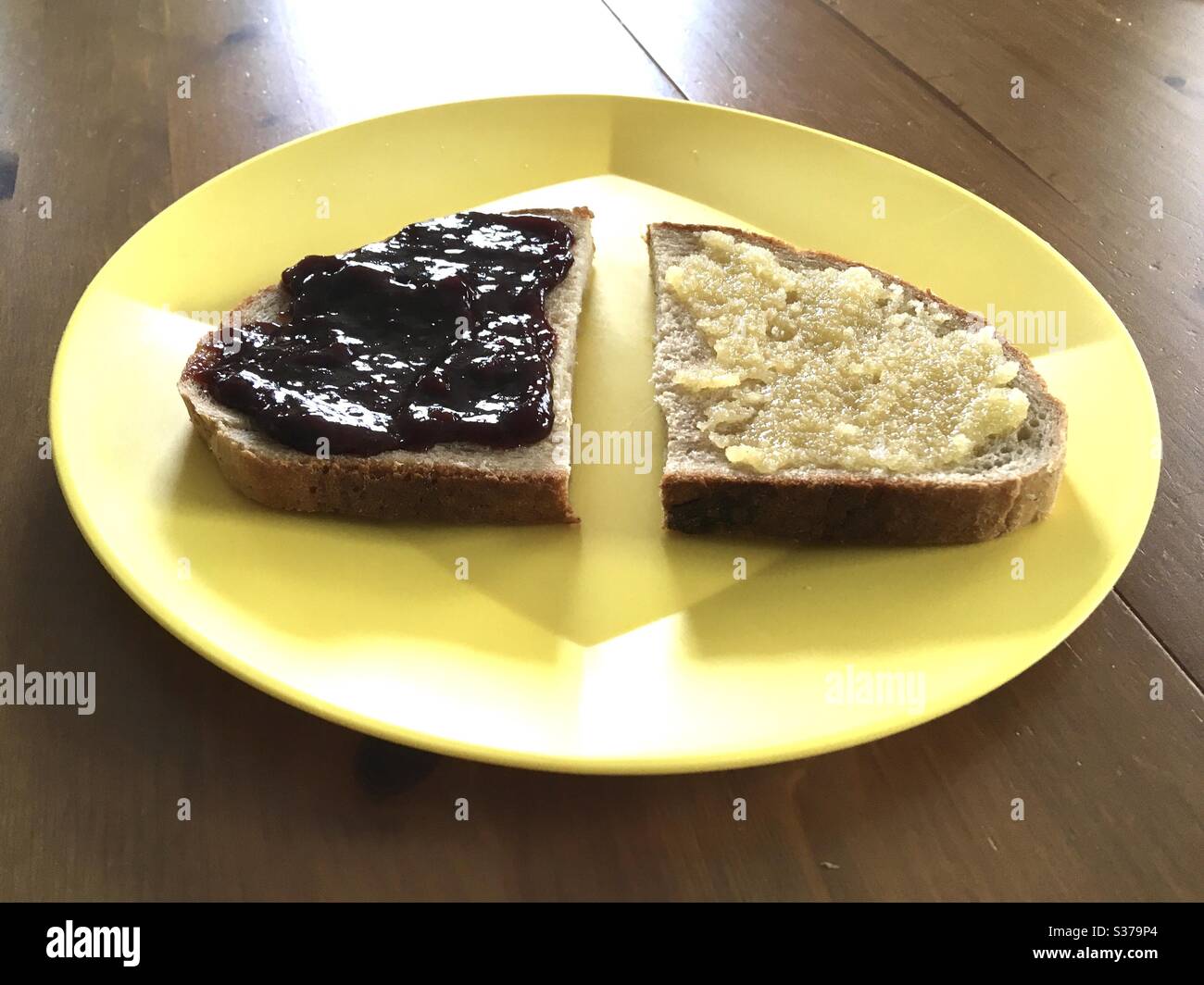 Brotscheibe in zwei Teile geteilt mit Pflaumenmarmelade und Honig auf gelbem Kunststoffteller Stockfoto