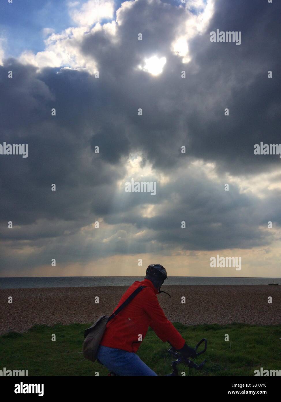 Ein Mann, der auf dem Radweg entlang der Promenade radelt und die Sonnenstrahlen, die durch die Wolken über dem Seedeal Kent UK kommen, betrachtet - Smartphone-aufgenommenes Stockfoto