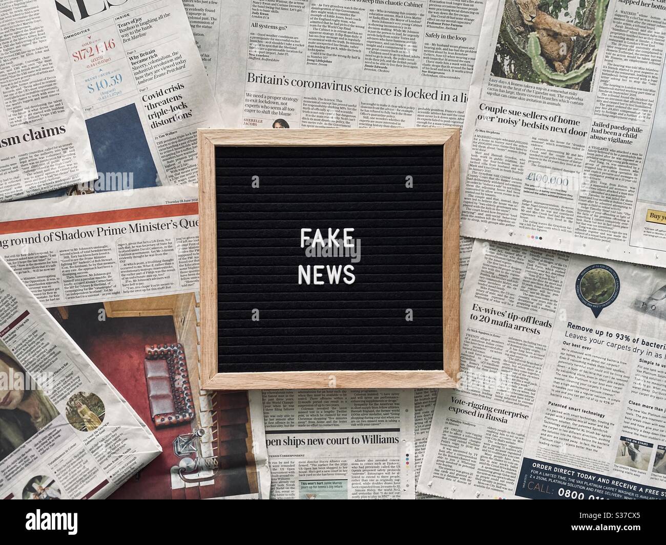 Eine Nahaufnahme einer schwarzen Filz-Tafel mit dem Ausdruck Fake News, gesehen vor einem Hintergrund nationaler Zeitungsseiten. Schlagzeilen, Boulevardblätter, Presse- und Medienkonzepte. Stockfoto