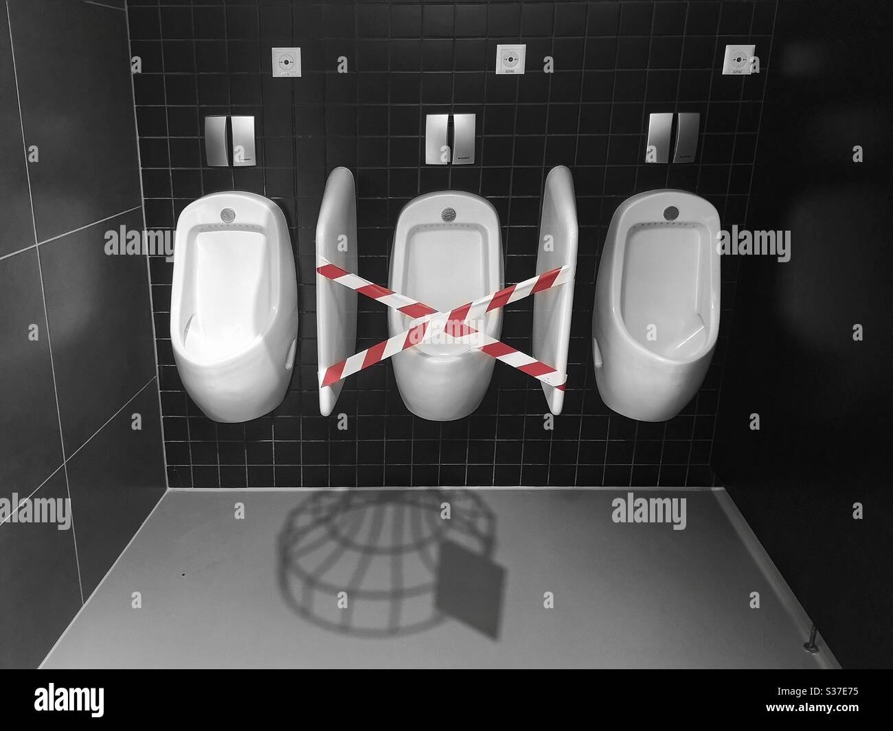 Soziale Distanzierung - mittleres Urinal im Satz von drei abgesperrt mit rotem und weißem Band Stockfoto