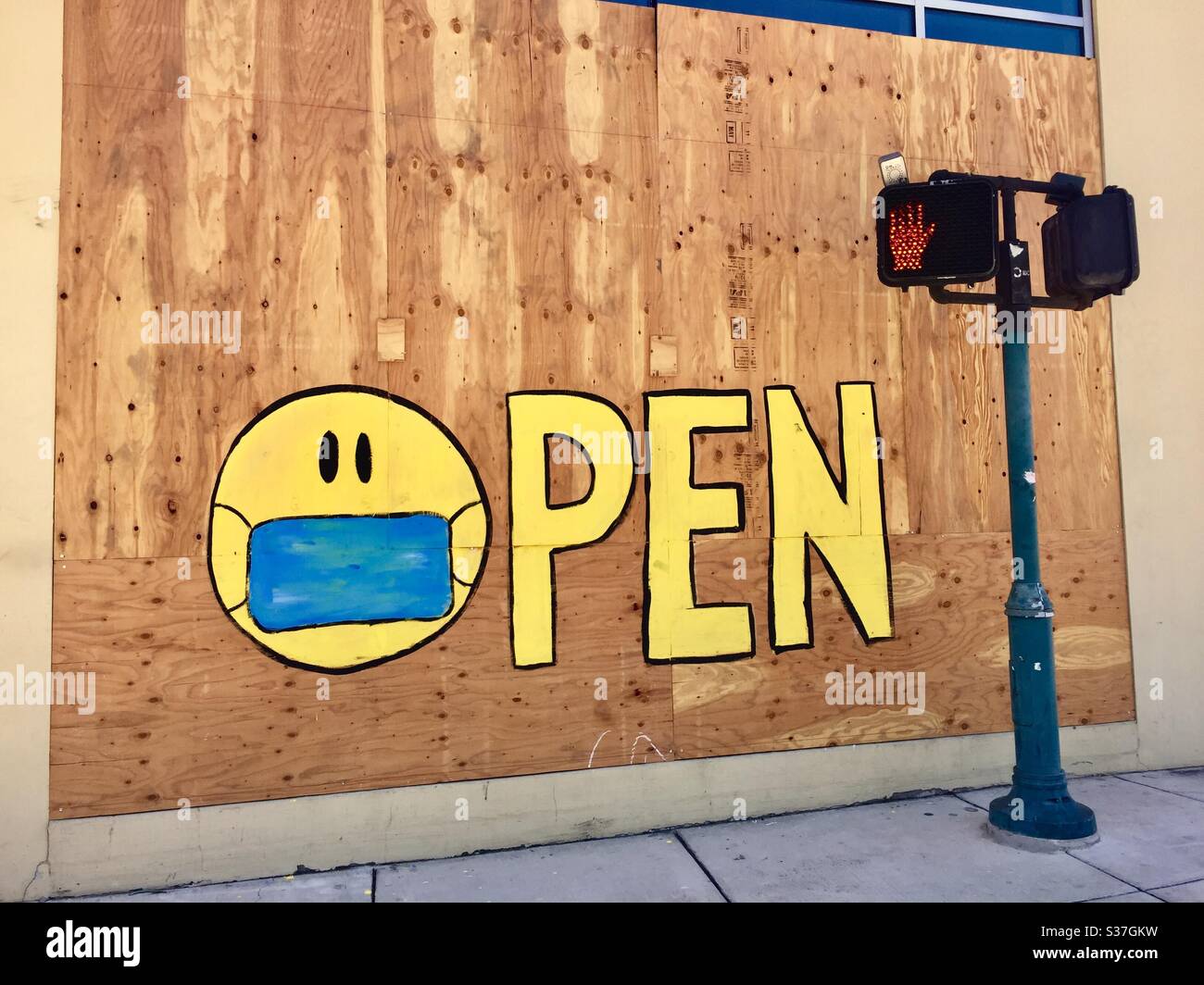 „Öffnen“-Schild auf einem vernagelten Fenster mit Smiley-Gesicht trägt eine medizinische Maske in der Nähe eines nicht gehen Zeichen. Stockfoto