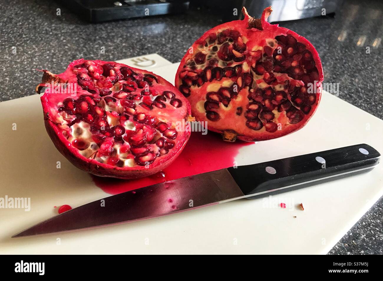 Granatapfel auf einem Schneidebrett mit einem Messer daneben aufschneiden - Smartphone-aufgenommenes Stockfoto