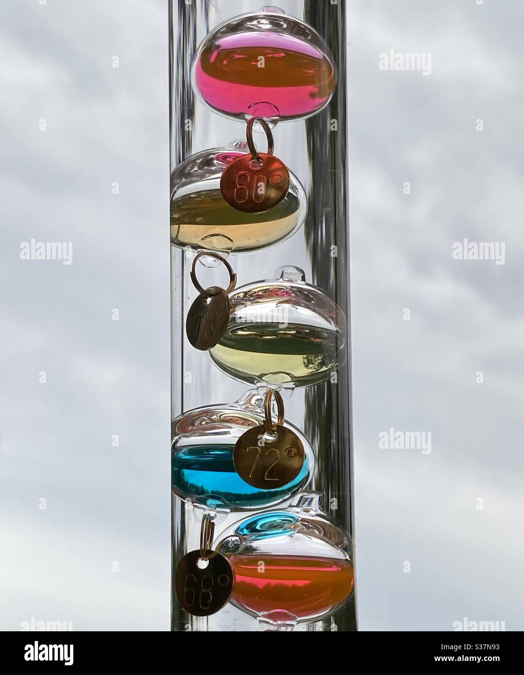 Ein farbenfrohes Wetterthermometer gegen grauen, wolkigen Himmel - Smartphone-aufgenommenes Stockfoto