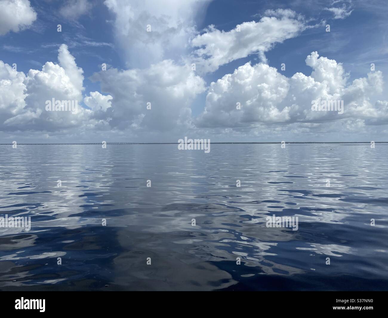 Weißer, wolkiger Himmel, der sich auf das blaue Wasser der Bucht spiegelt - Smartphone-aufgenommenes Stockfoto