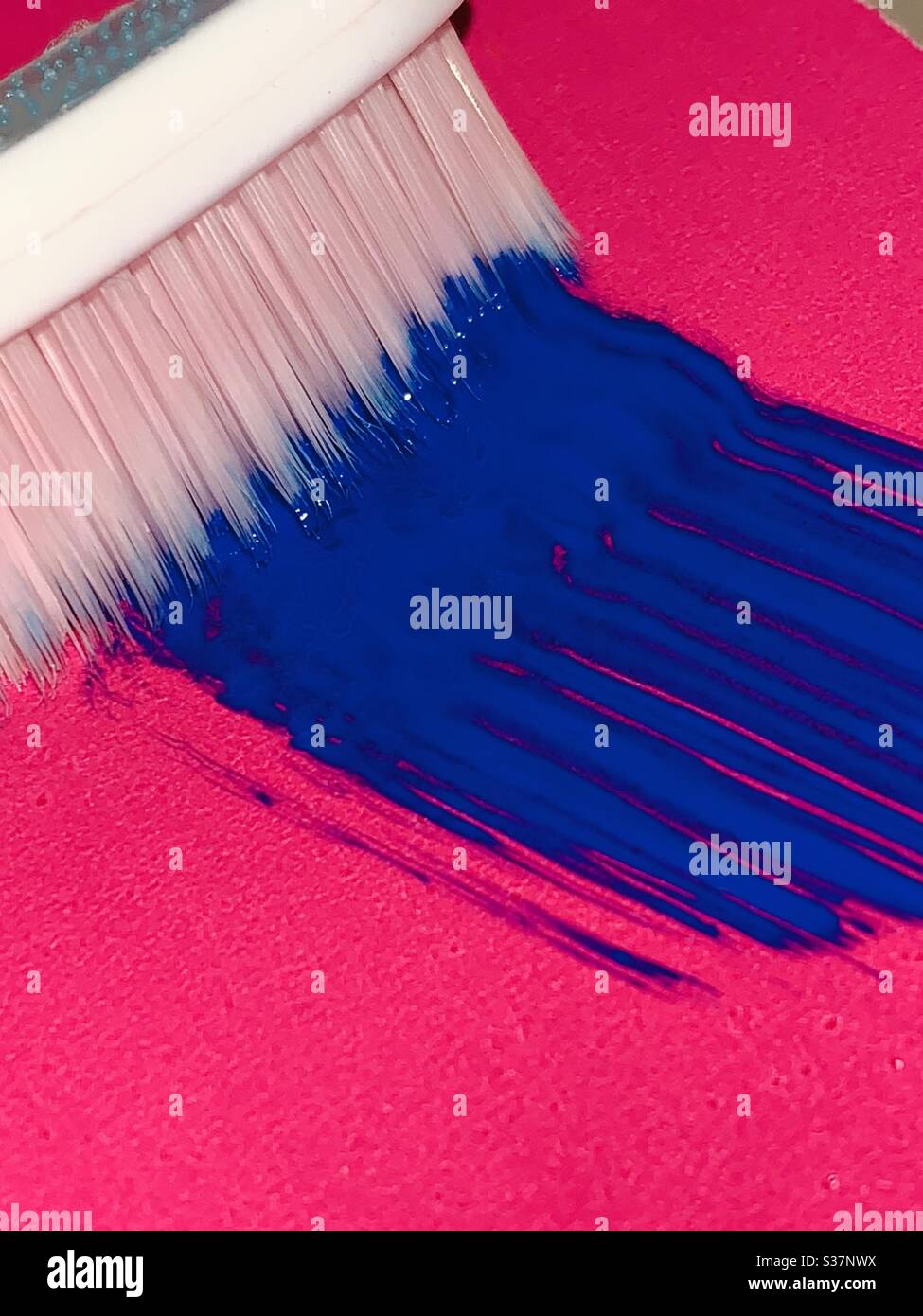 Blaue Farbe kommt von Pinsel auf magentafarbenem Papier Stockfoto