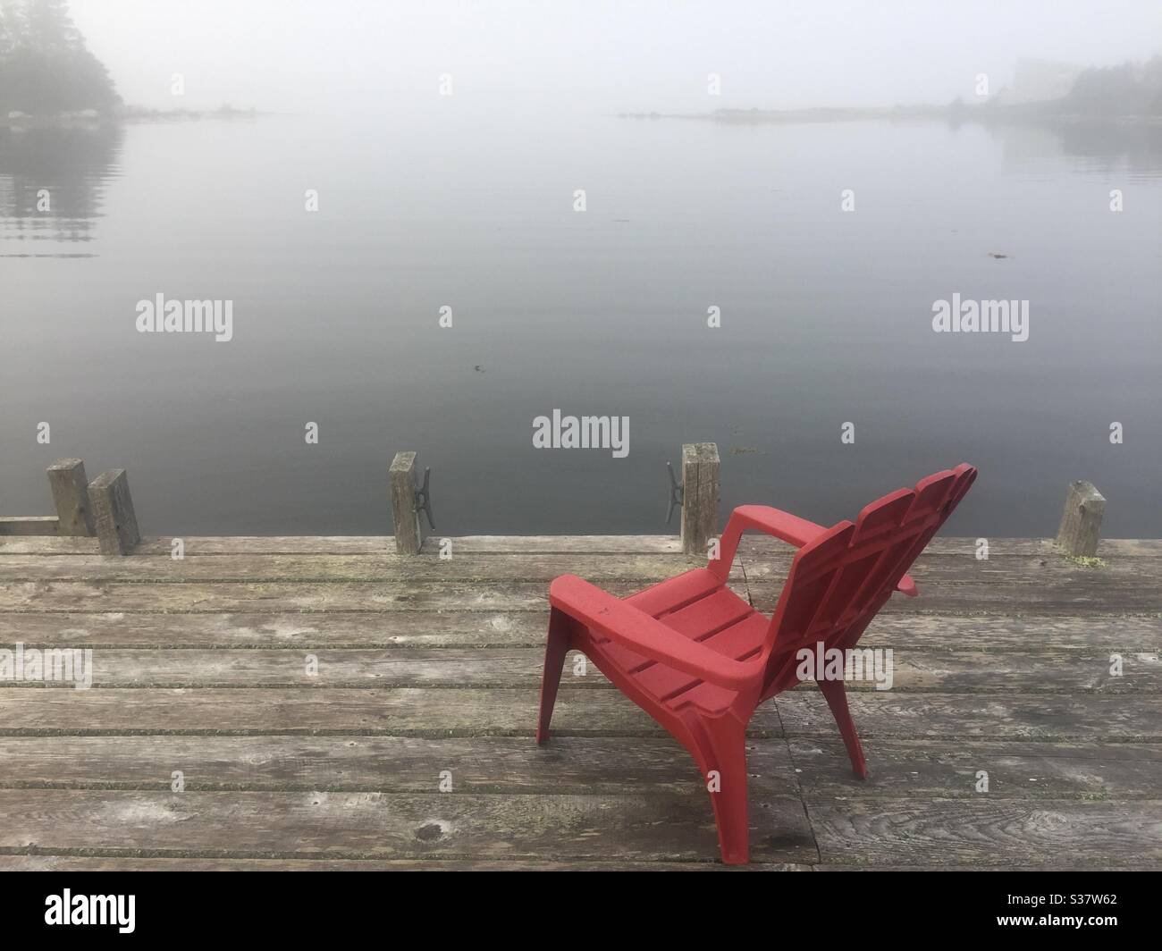 Leerer roter Stuhl am Dock, Nebel rollt ein, Halifax, Nova Scotia, Kanada. Konzepte: einsamkeit, heißer Sitz, Kraft des Einen, drohende Düsternis, Untergang. Stockfoto