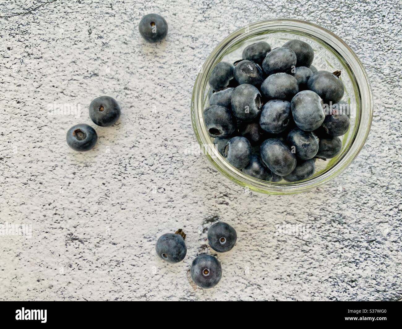Nahaufnahme von frischen Blaubeeren in einer kleinen Glasschüssel gegen eine natürliche Granitplatte in der Küche. Saftige Beeren voller Antioxidantien - Smartphone-aufgenommenes Stockfoto