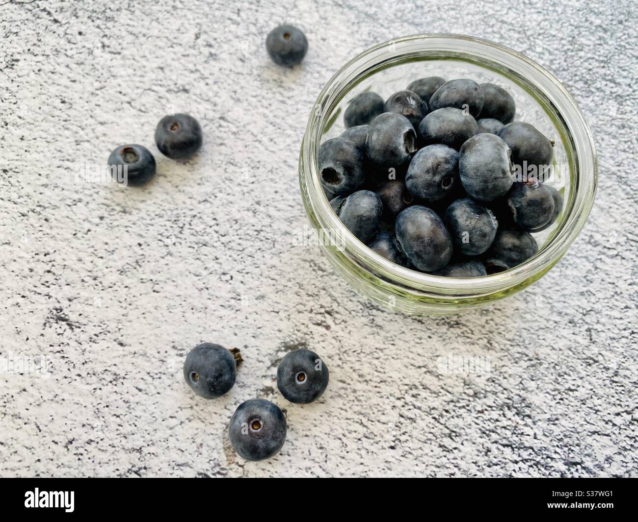 Nahaufnahme von frischen Blaubeeren in einer kleinen Glasschüssel gegen eine natürliche Granitplatte in der Küche. Saftige Beeren voller Antioxidantien - Smartphone-aufgenommenes Stockfoto
