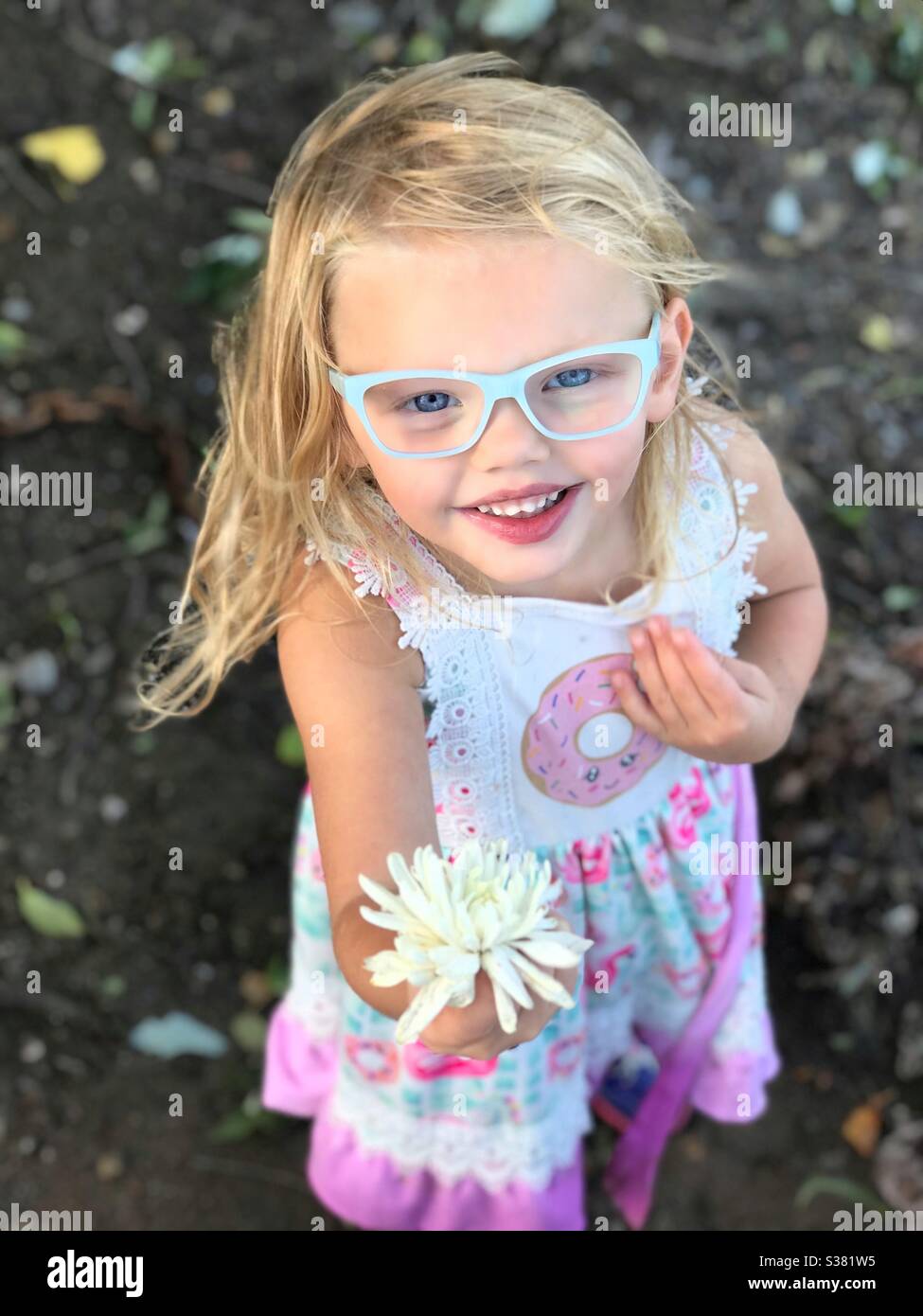 Kleines Mädchen zeigt eine Blume, die sie gefunden hat. Aufgeregt mit einem Lächeln. Stockfoto