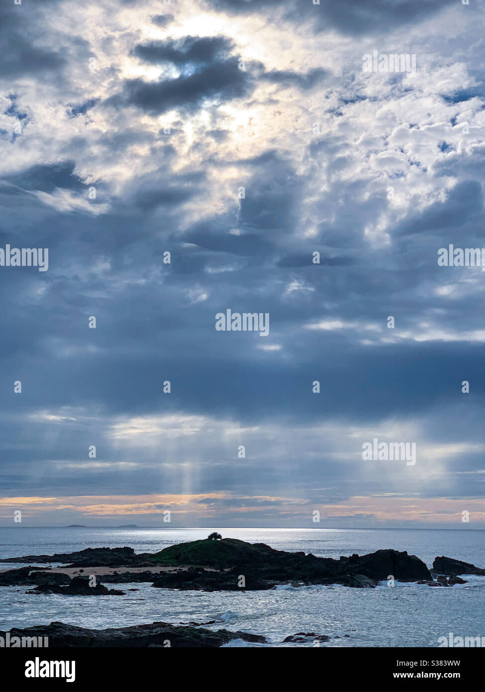Strahlen von Sonnenstrahlen, die von den Sturmwolken über dem Ozean herabströmen. Sonnenlicht schimmert auf dem Ozean - Smartphone-aufgenommenes Stockfoto