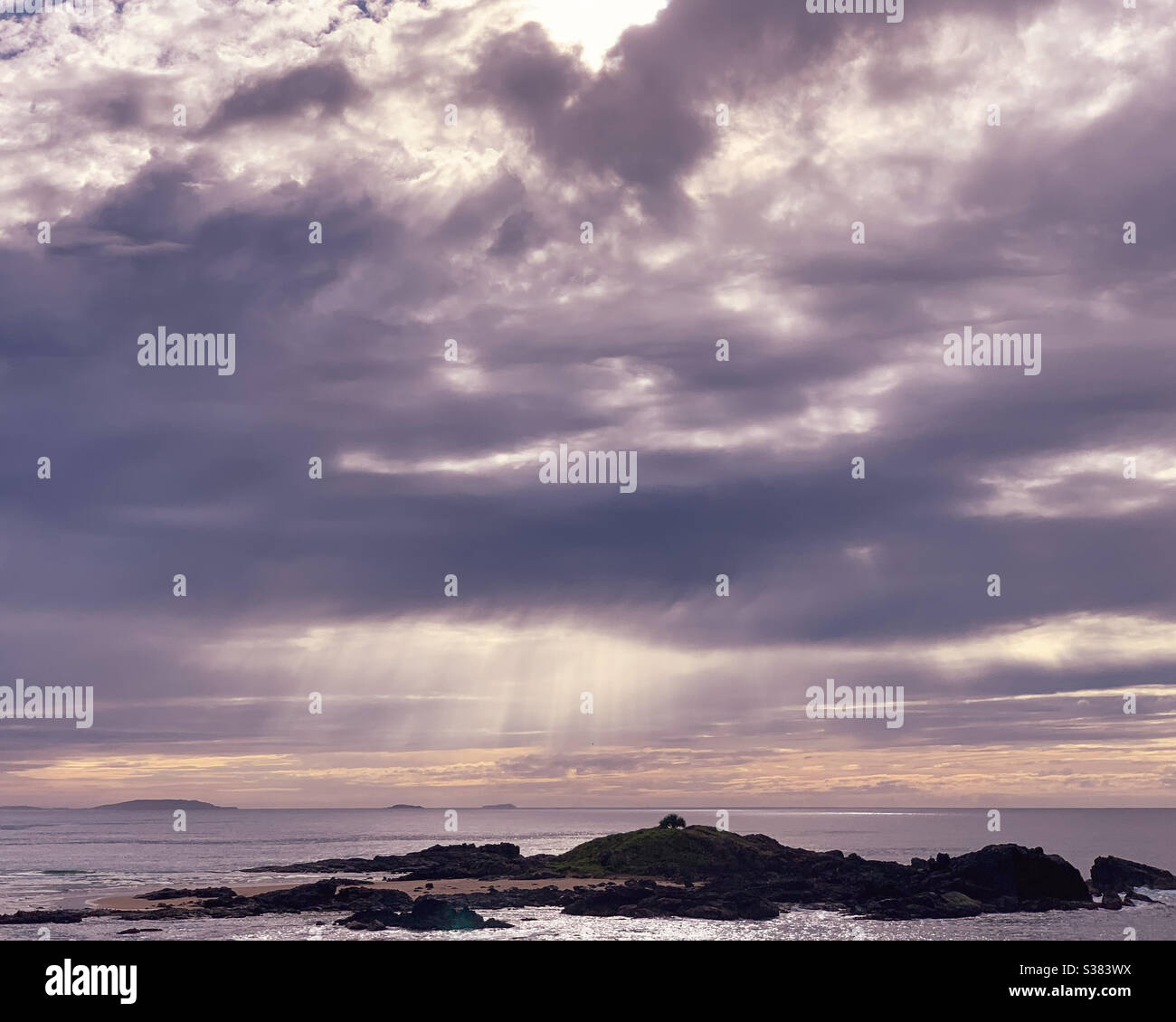 Ätherische Sonnenstrahlen, die durch ein Loch in den Sturmwolken über dem Meer platzen, auf das Meer darunter - Smartphone-aufgenommenes Stockfoto