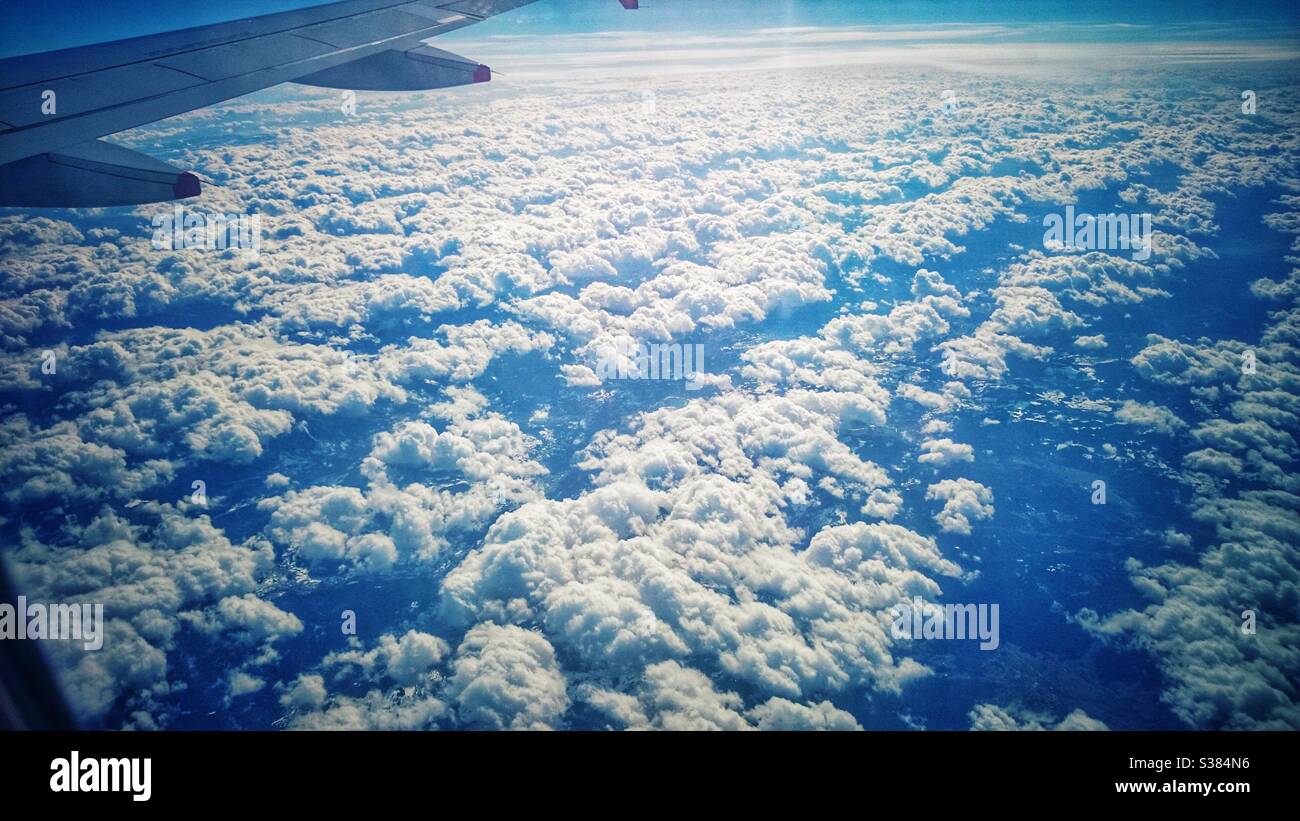 Ein Foto, das aus einem Flugzeug über schöne, flauschige weiße Wolken blickt. Stockfoto