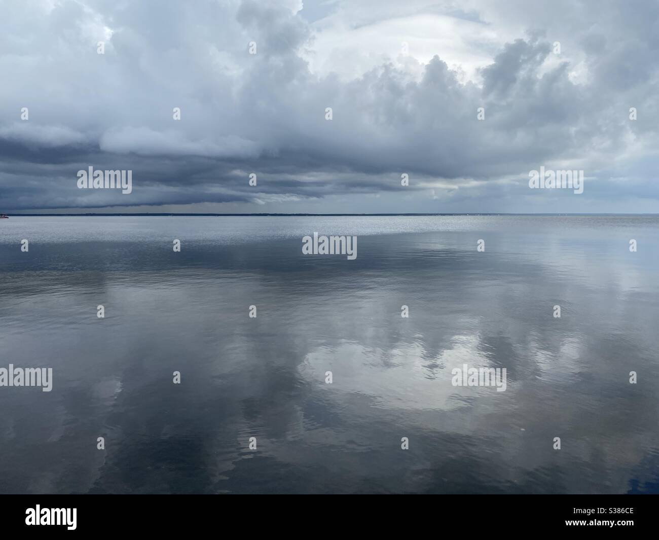 Stürmischer Himmel, der sich auf das noch immer in der Bucht spiegelnde Wasser spiegelt - Smartphone-aufgenommenes Stockfoto