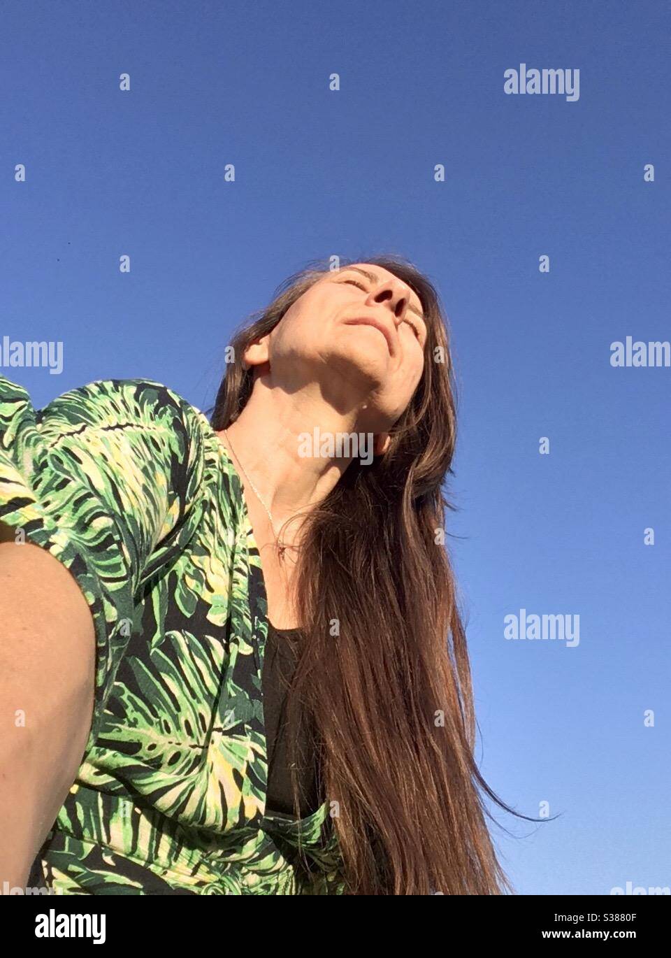 Selfie, Frau mit langen geraden Haaren in hellen Sommerkleid genießen die Sonne scheint auf ihrem Gesicht mit dem perfekten blauen Himmel als Hintergrund, Model Release verfügbar Stockfoto