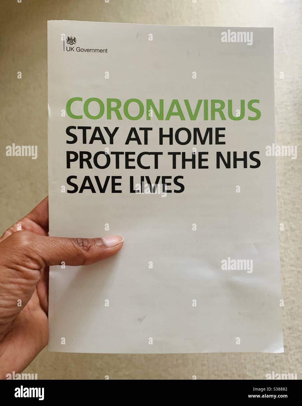 Eine Hand mit einem Coronavirus-Bleib zu Hause Flugblatt der britischen Regierung Stockfoto