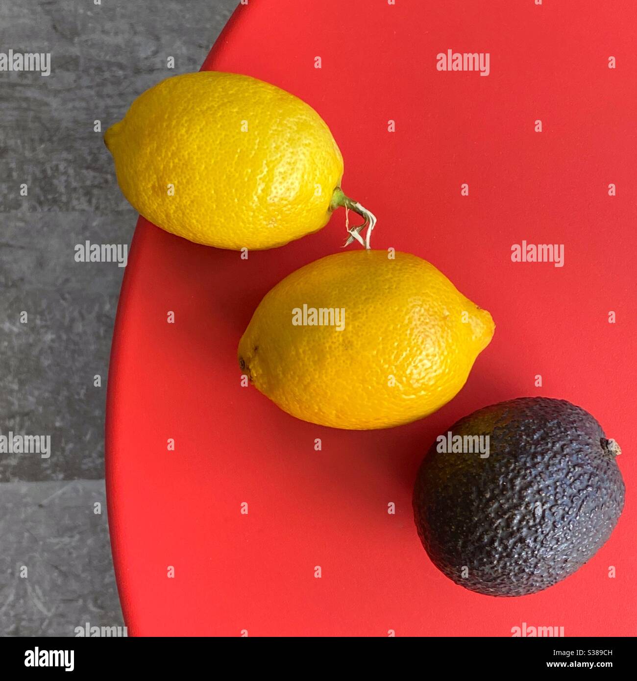 Zwei Zitronen und eine Avocado auf einem roten Tisch Stockfoto