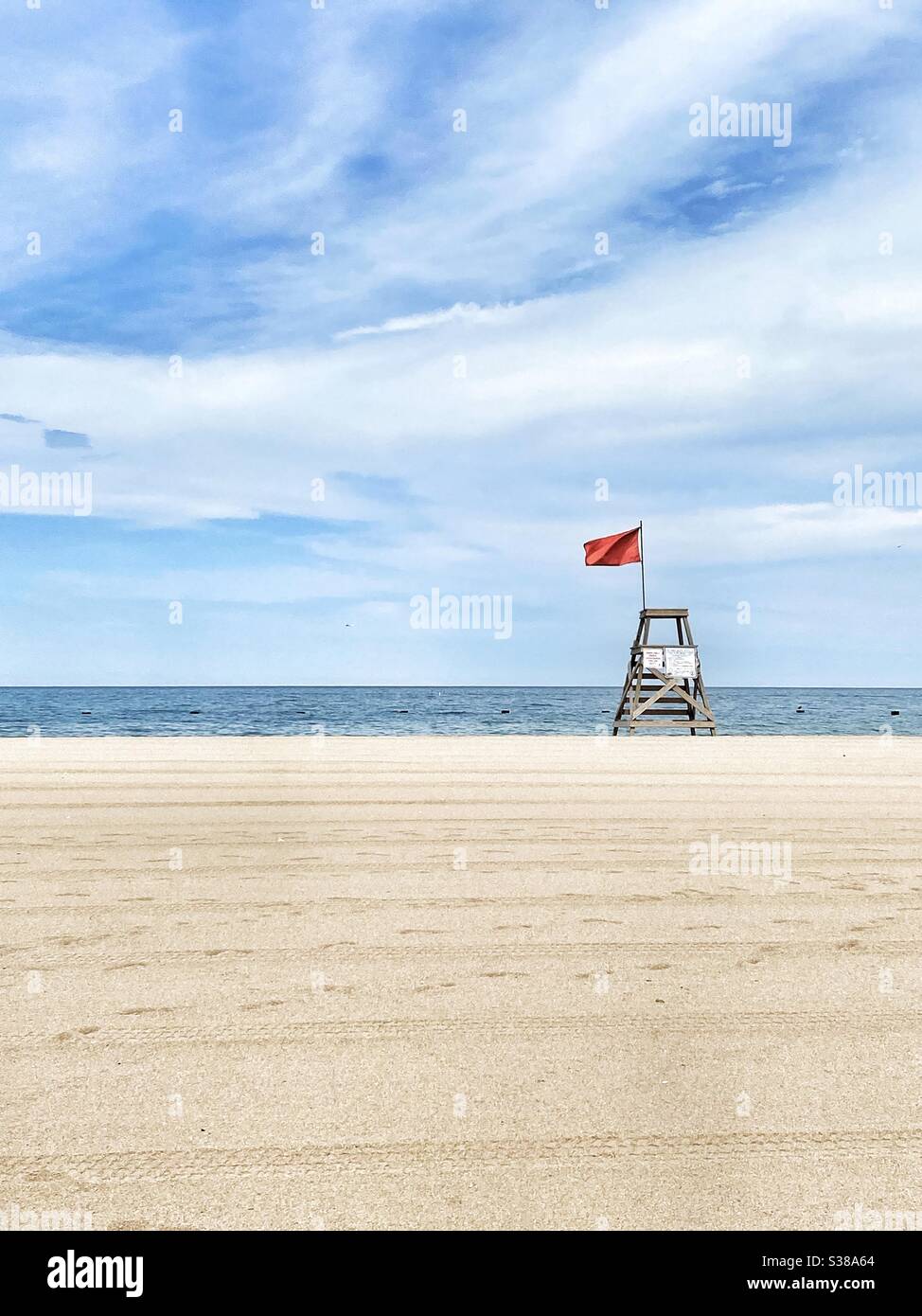 Leerer Strand mit leerstehender Rettungsschwimmerstation mit roter Flagge, die das Schwimmen im Wasser verbietet Stockfoto