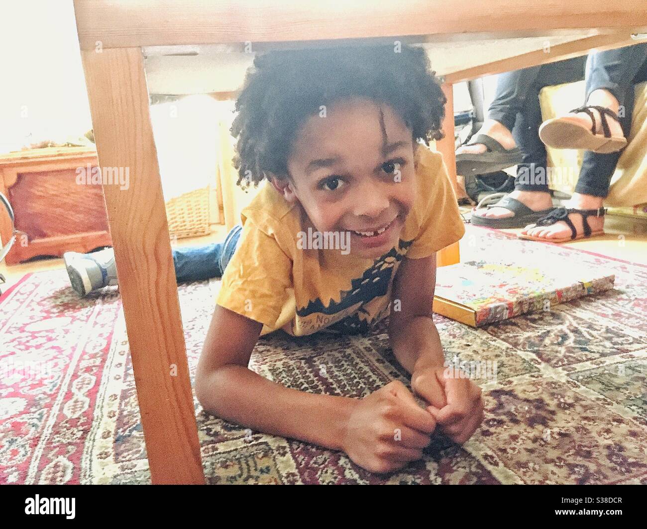 Ein kleiner Junge, der unter einem Tisch spielt. Stockfoto