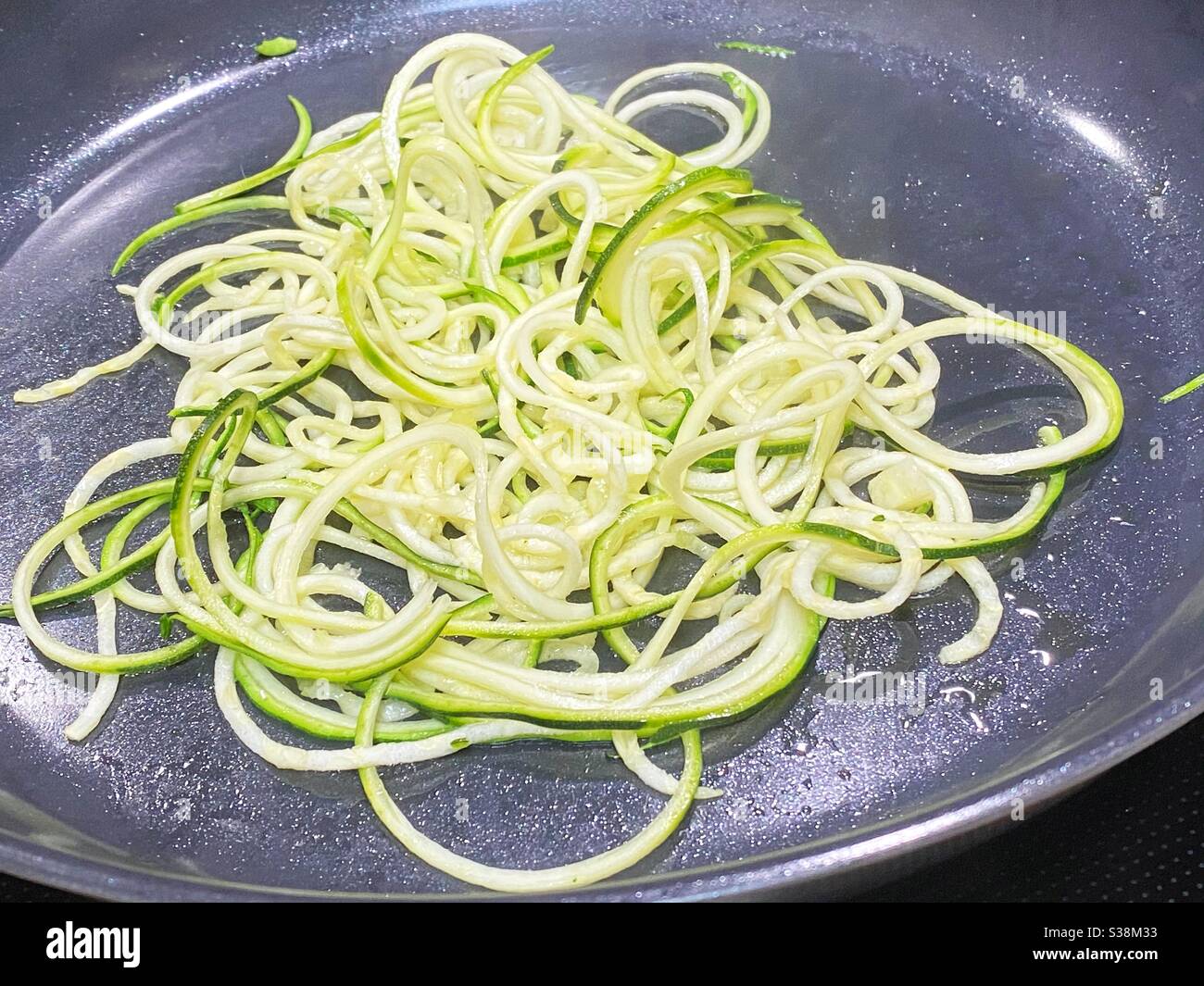 Spiralisierte Zucchini 'Nudeln' werden sautiert. Stockfoto