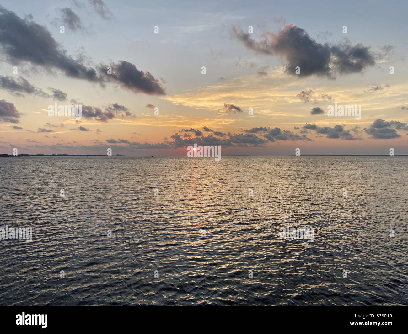 Leuchtend rote Sonne, die tief am Horizont über der Bucht liegt Wasser bei Sonnenuntergang Stockfoto