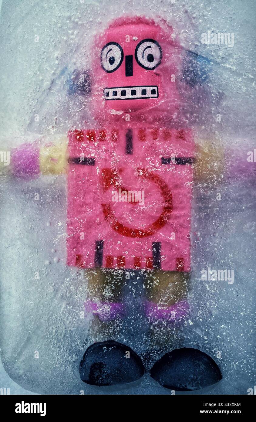 Ein rosafarbener und schwarzer Holzspielzeug-Roboter starrt aus Ein Eisblock Stockfoto