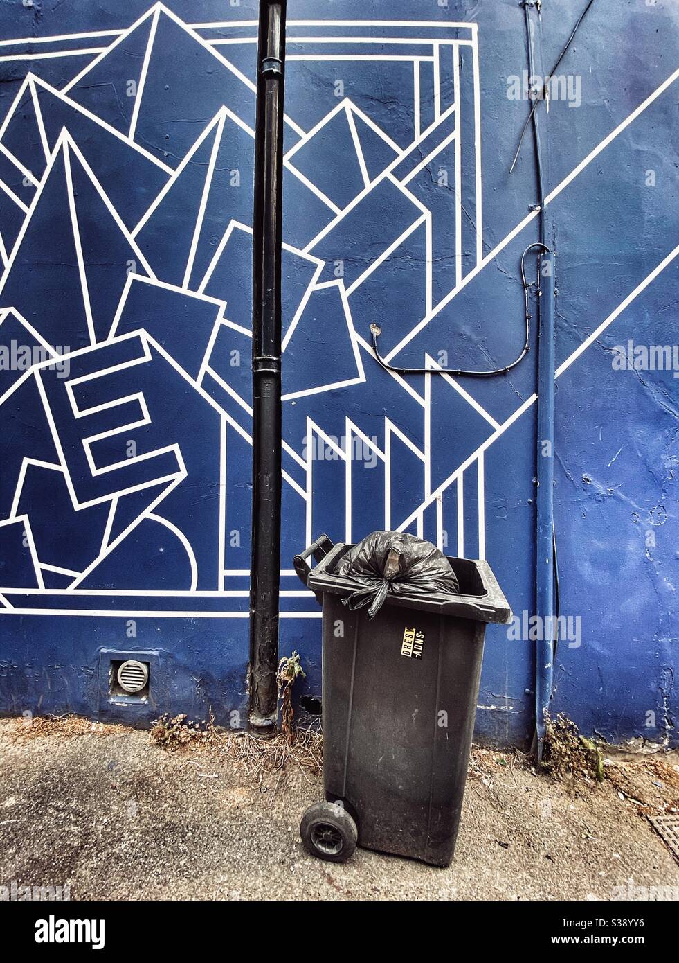 Eine Mülltonne vor einer abstrakten Wand Stockfoto