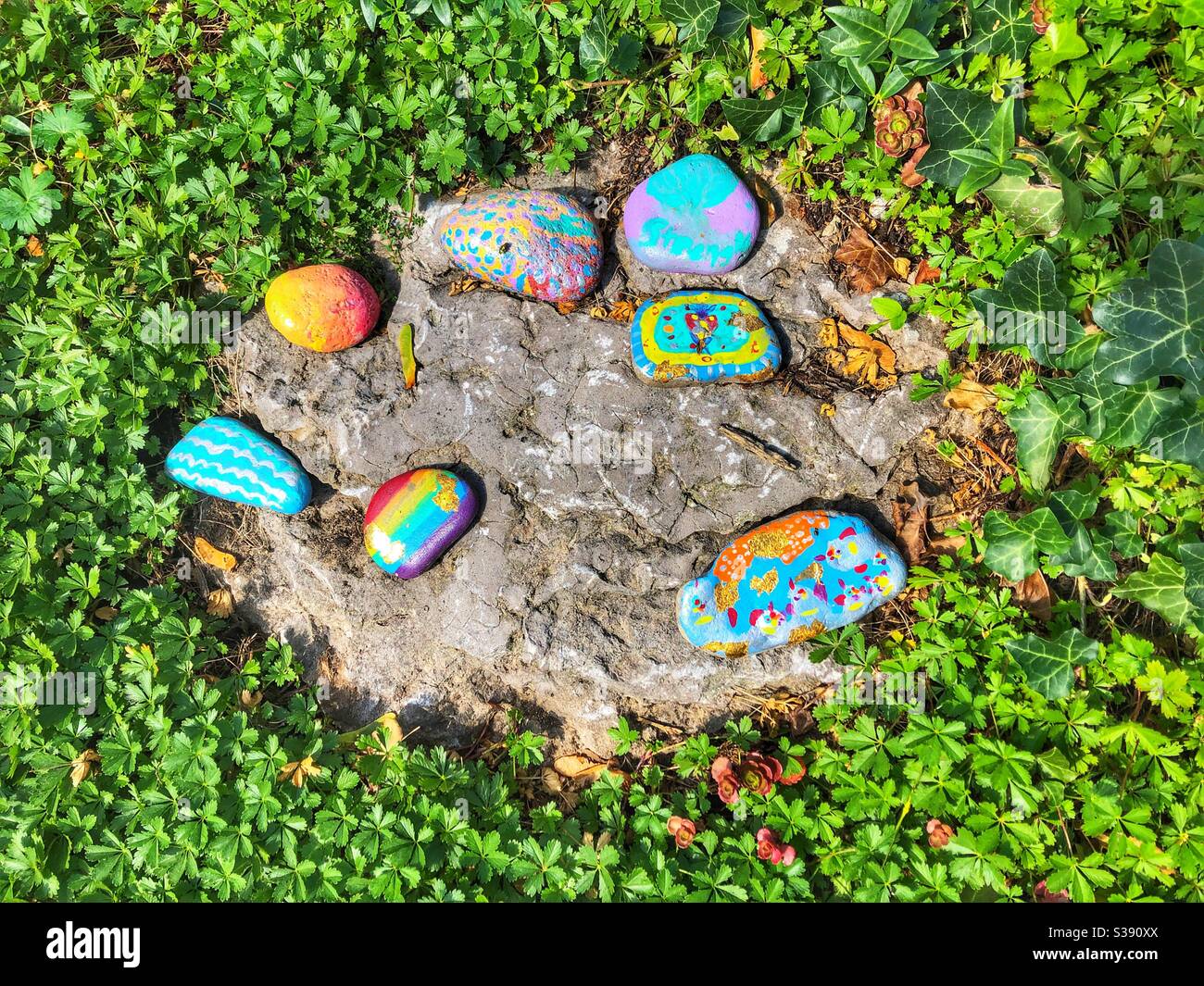 Bunt bemalte Steine auf einem Gartenfelsen zur Dekoration platziert. - Smartphone-aufgenommenes Stockfoto