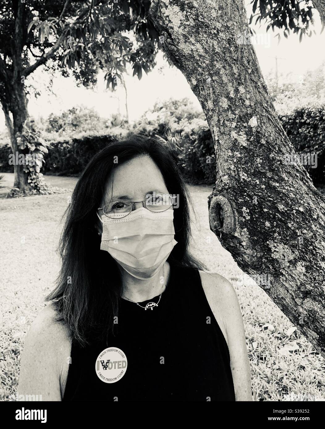 Frau, die gerade während der COVID-19 in der lokalen Primärwahl gestimmt hat, trägt einen Sticker und eine nicht-chirurgische Maske. Stockfoto