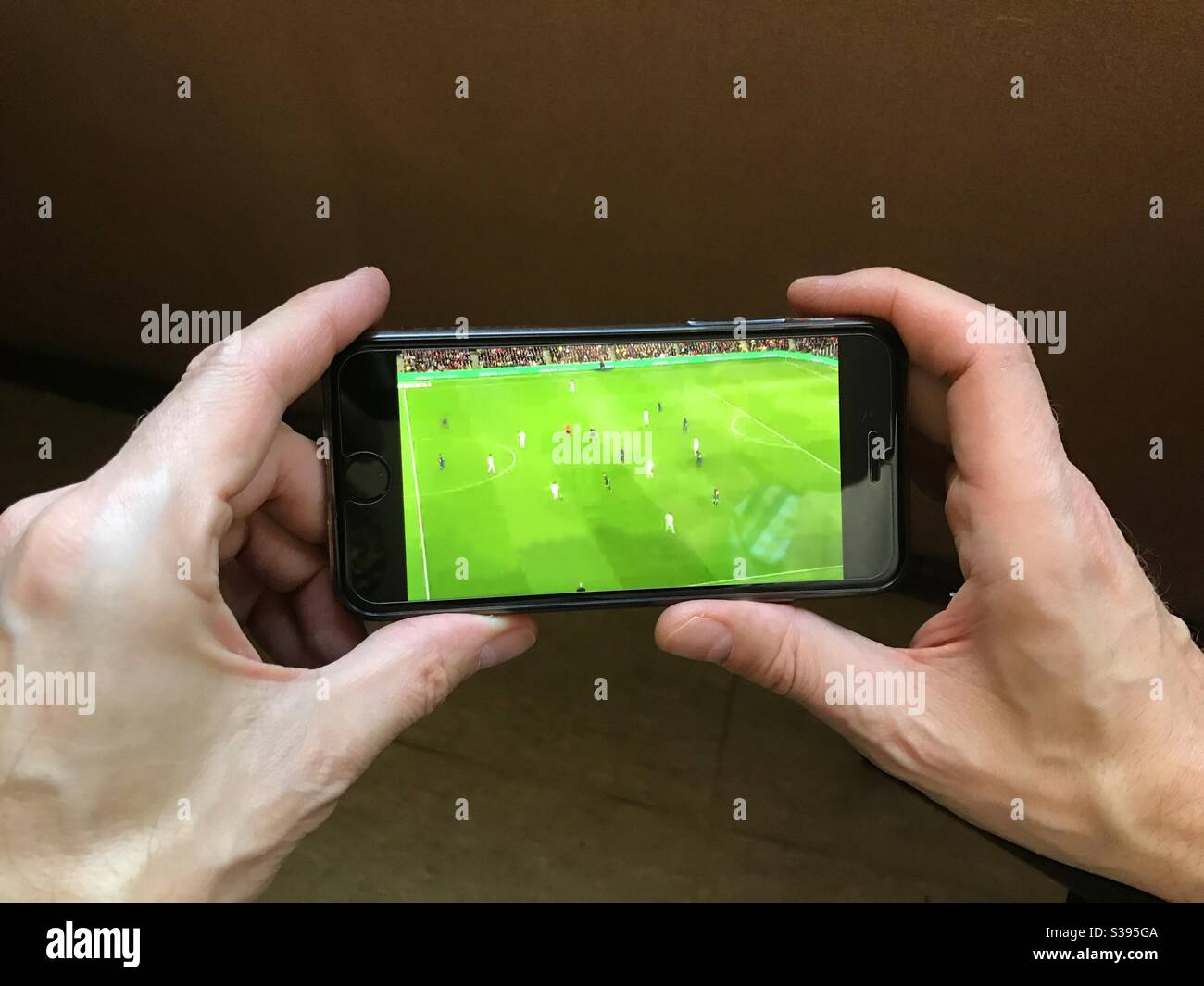 Hände halten ein Smartphone, zeigt ein Fußballspiel - Smartphone-aufgenommenes Stockfoto