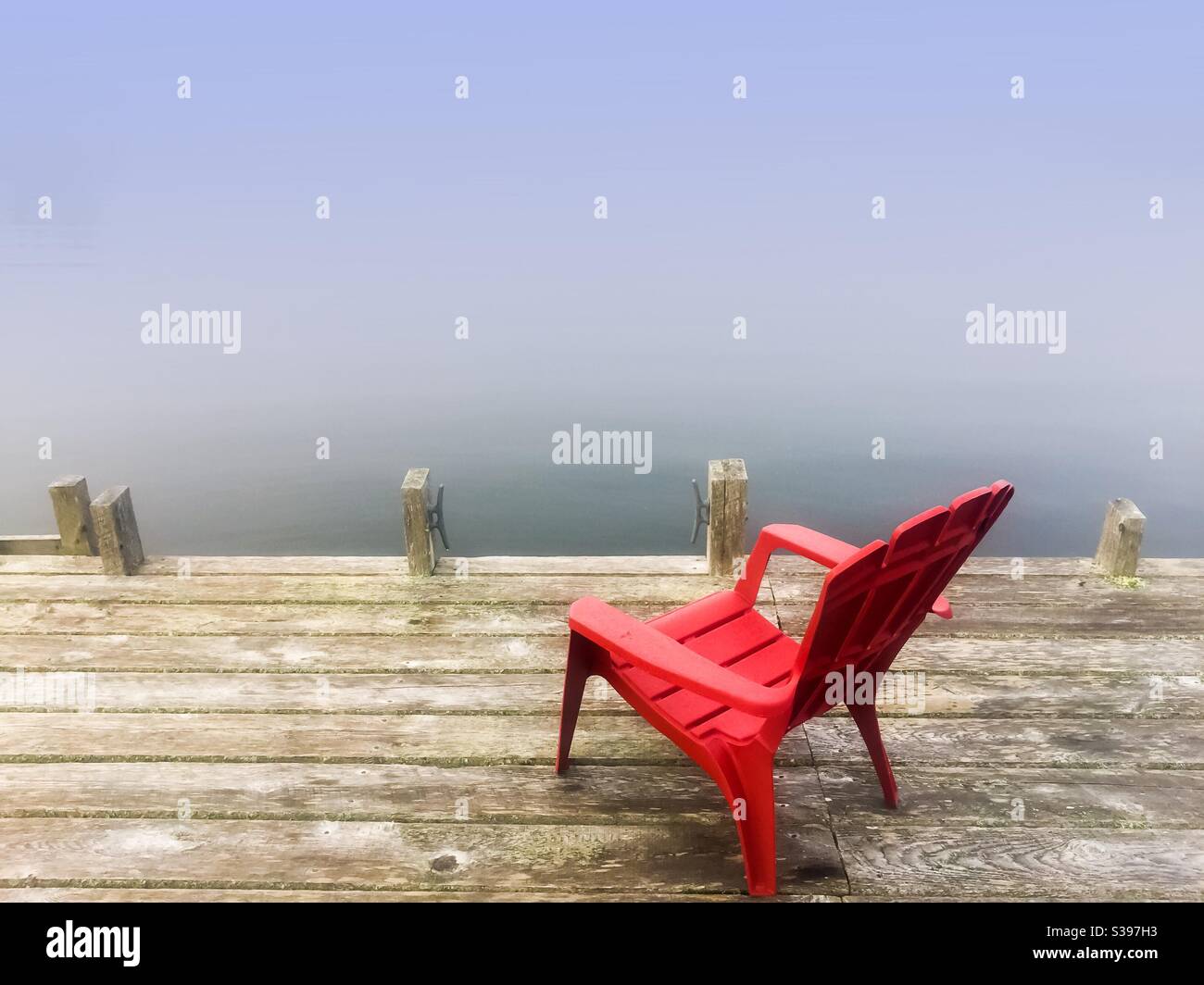 Ein Stuhl auf einem Dock im Nebel mit Blick auf das Wasser, Nova Scotia, Kanada. Zimmer für Typ. Konzeptuelles Bild, das Einsamkeit, Kraft eines Menschen, heiße Sitzfläche, herannahender Nebel zeigt. Stockfoto