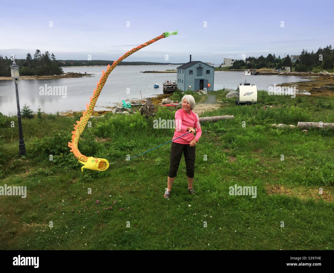 Spritziger Senior mit einem tanzenden Drachen am Meer, Halifax, Nova Scotia, Kanada. Auf Gras, mit Blick auf das Meer. Ein Tag am blauen Himmel. Stockfoto