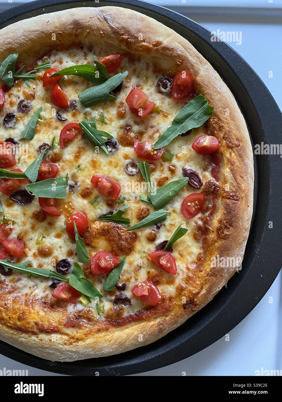 Hausgemachte Pizza mit Oliven, Tomaten und Rucola Stockfoto
