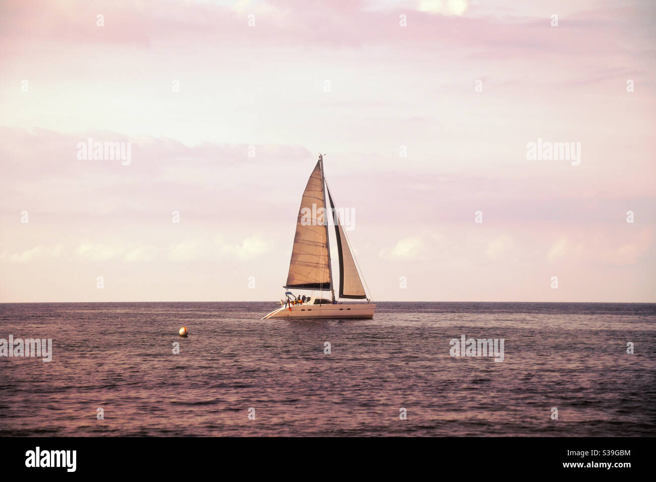 Katamaran im Profil im mystischen Flieder Abend Licht und wolkiger Himmel an der Ostseeküste. Neben dem Boot kann man eine Boje sehen Stockfoto